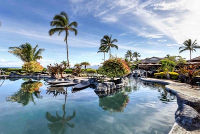 Crystal-clear water mirrors the vibrant blue sky above. The Hali‘i Kai pool is a visual and sensory retreat.
