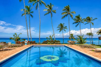 Oceanfront pool at Mahina Surf — hibiscus-tiled pool framed by swaying palms with views toward Lanai and Molokai