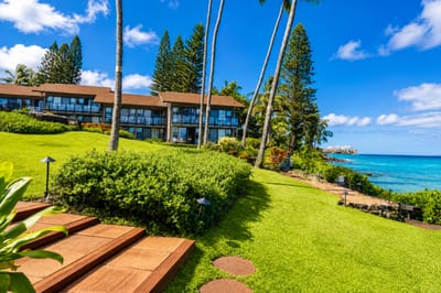 Grounds at Mahina Surf — tiered lawns and Norfolk pines step down to the ocean, with West Maui's coastline visible in the distance