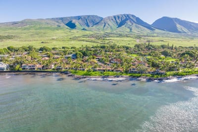 Breathtaking aerial of oceanfront villas framed by lush tropical grounds & panoramic island mountain views
