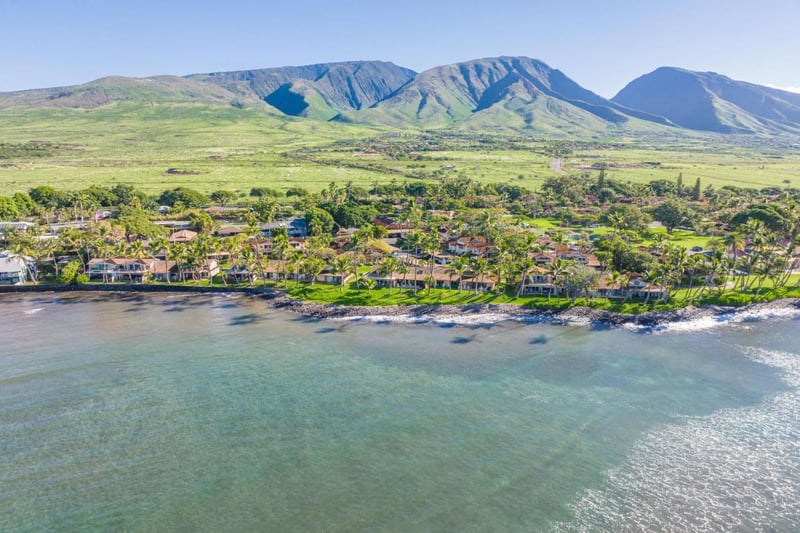 Breathtaking aerial of oceanfront villas framed by lush tropical grounds & panoramic island mountain views
