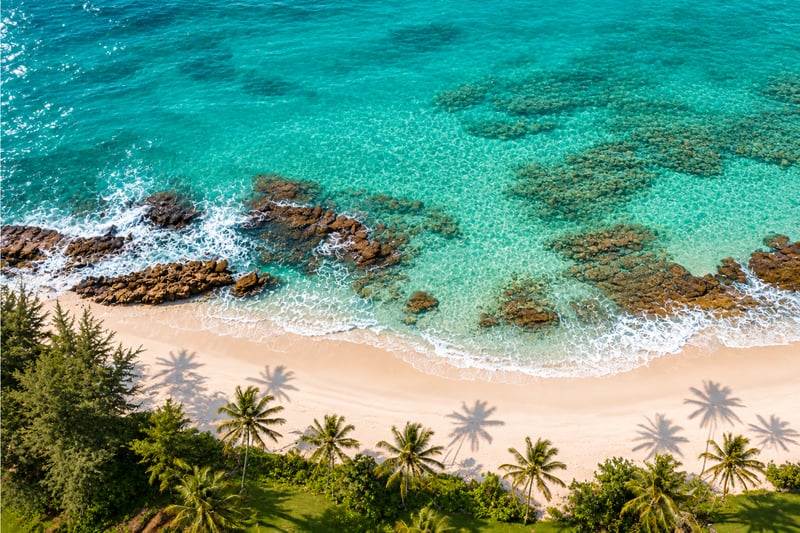 Aerial look at the rugged shoreline near Kuilima Estates, where turquoise waves crash against lava rock and forested cliffs frame Oahu’s wild North Shore.