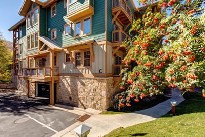 Charming mountain condo with lush landscaping, stone accents, and colorful autumn trees lining the drive. TPC-102C
