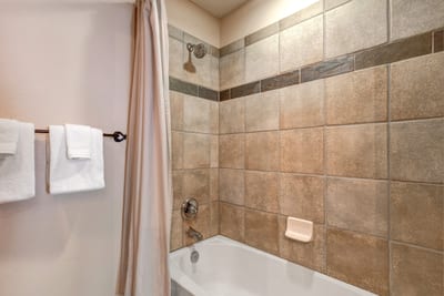 This tiled shower/tub combo features warm stone tones, soft towels, and easy access from Guest Bedroom 1.