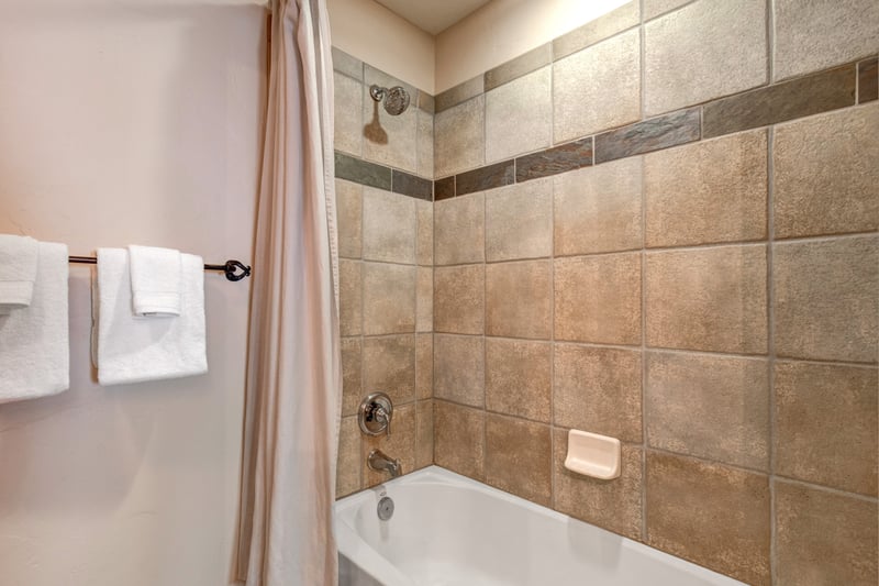 This tiled shower/tub combo features warm stone tones, soft towels, and easy access from Guest Bedroom 1.