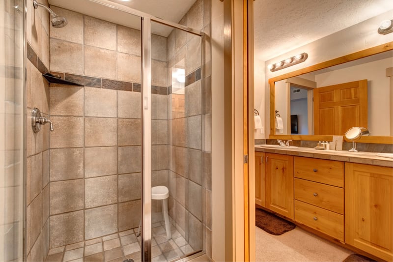 The primary ensuite features a tiled walk-in shower, granite double vanity, and wood cabinetry with warm mountain character.
