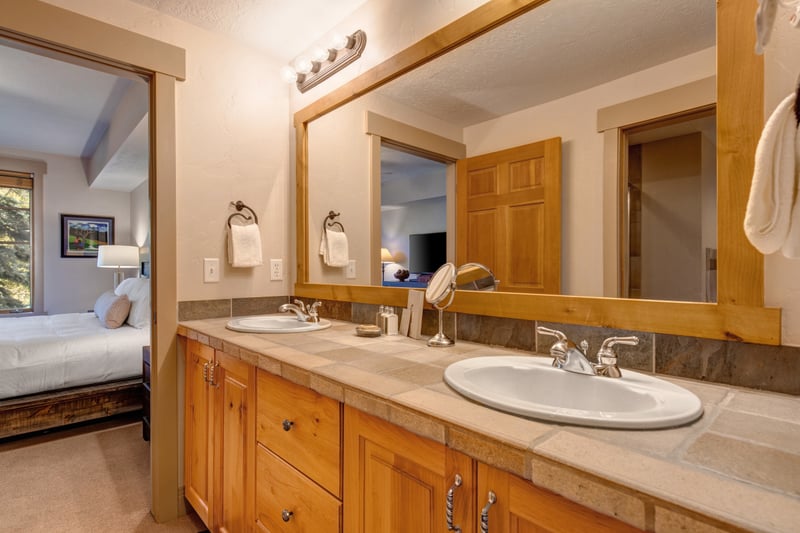 The ensuite bath includes a granite double vanity, natural wood cabinetry, and a peek into the serene bedroom retreat.
