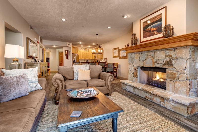 This open-concept living area features a stone fireplace, warm lodge-style accents, and flow to the dining and kitchen spaces.