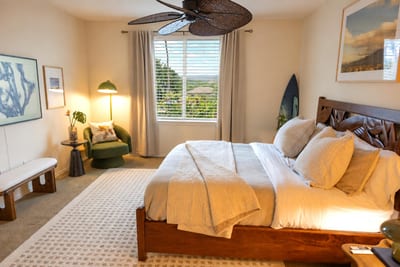 A serene primary bedroom with a king bed, layered linens and tropical views through the plantation-style blinds FVW-L21