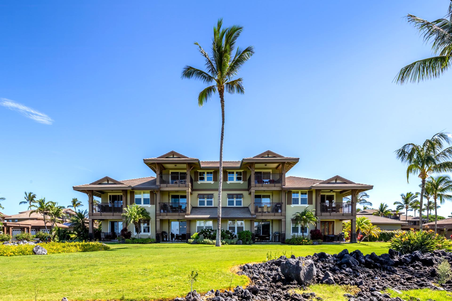 Lush green lawn fronts tropical condos beneath clear blue sky.