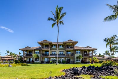 Lush green lawn fronts tropical condos beneath clear blue sky. HLI-12A