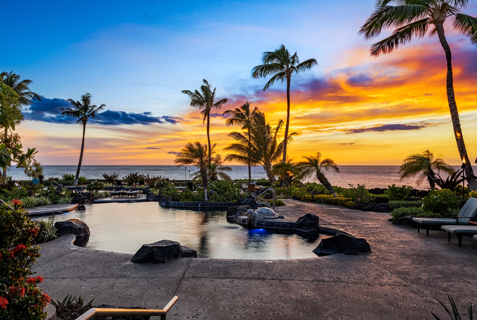 Swim beneath swaying palms in the lagoon-style pool, surrounded by tropical landscaping and cushioned loungers.