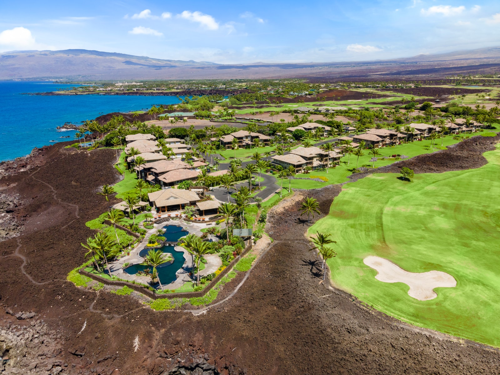 Aerial view showcases the resort’s oceanfront location, framed by lava rock, fairways, and lush grounds.