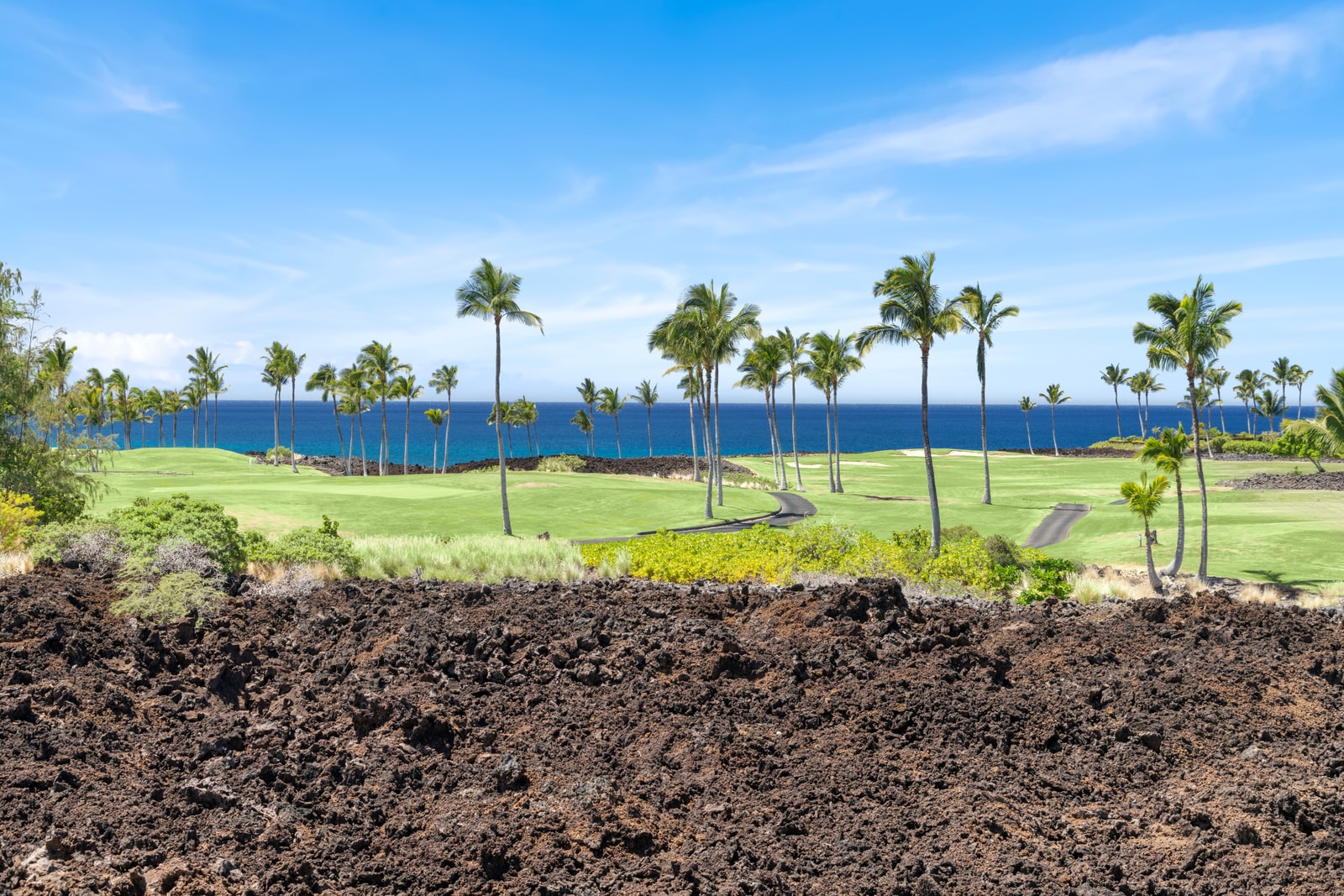 Lava rock and sweeping green fairways frame partial ocean views from the resort’s picturesque grounds.