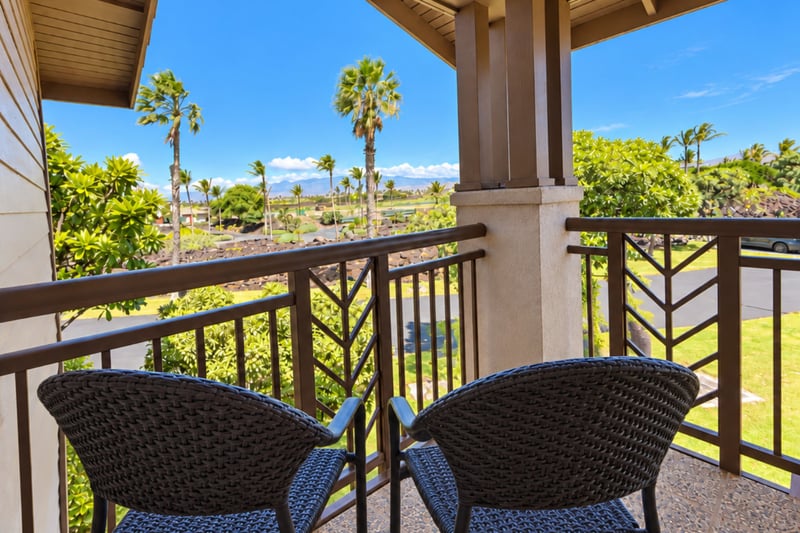 Upstairs balcony with two woven chairs overlooking palms and green lawns, with mountains rising in the distance.