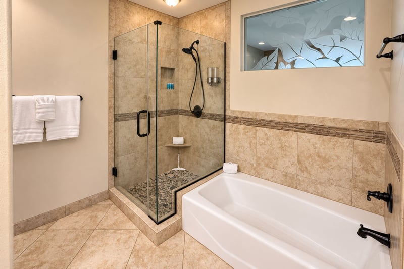 Primary bathroom with a glass enclosed corner shower and a separate tub beneath a frosted leaf window.
