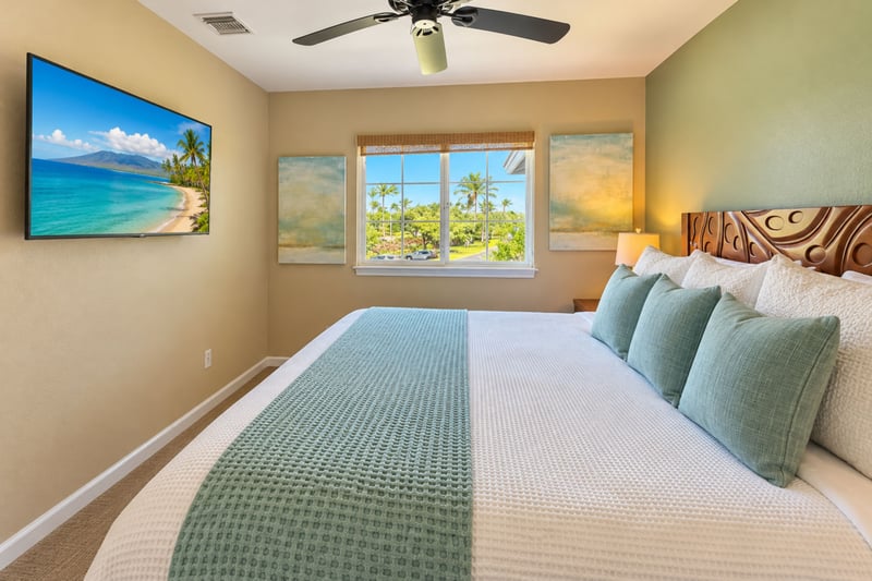Bedroom with a king bed, wall-mounted TV, and a window overlooking palm trees.