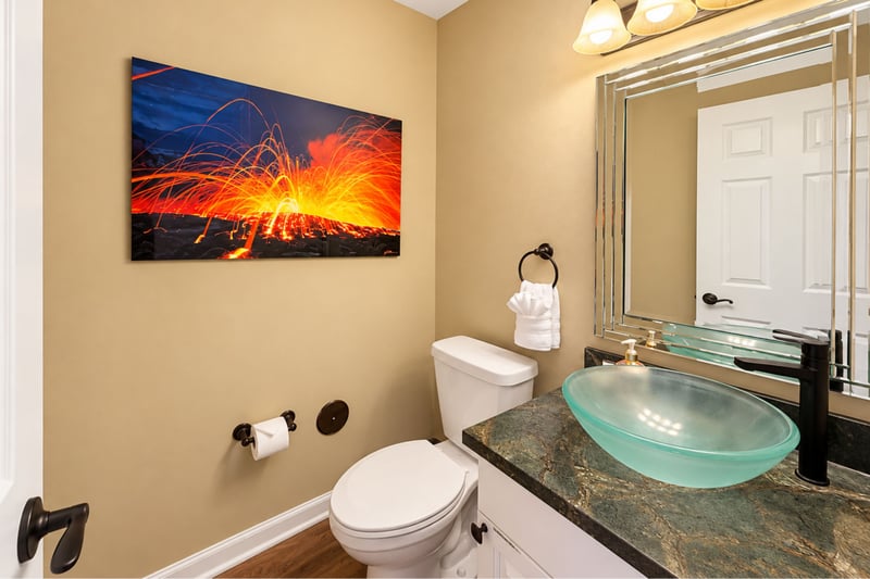 Half bathroom with a glass vessel sink, a framed mirror, and volcano artwork above the toilet.