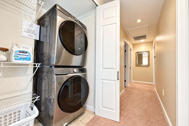 Stacked washer and dryer in a hallway closet, with shelving and a laundry basket for longer stays.