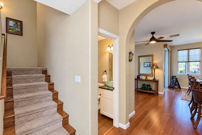 Carpeted staircase leading up to the bedroom level, with the half bathroom and the dining area visible through the arched opening.