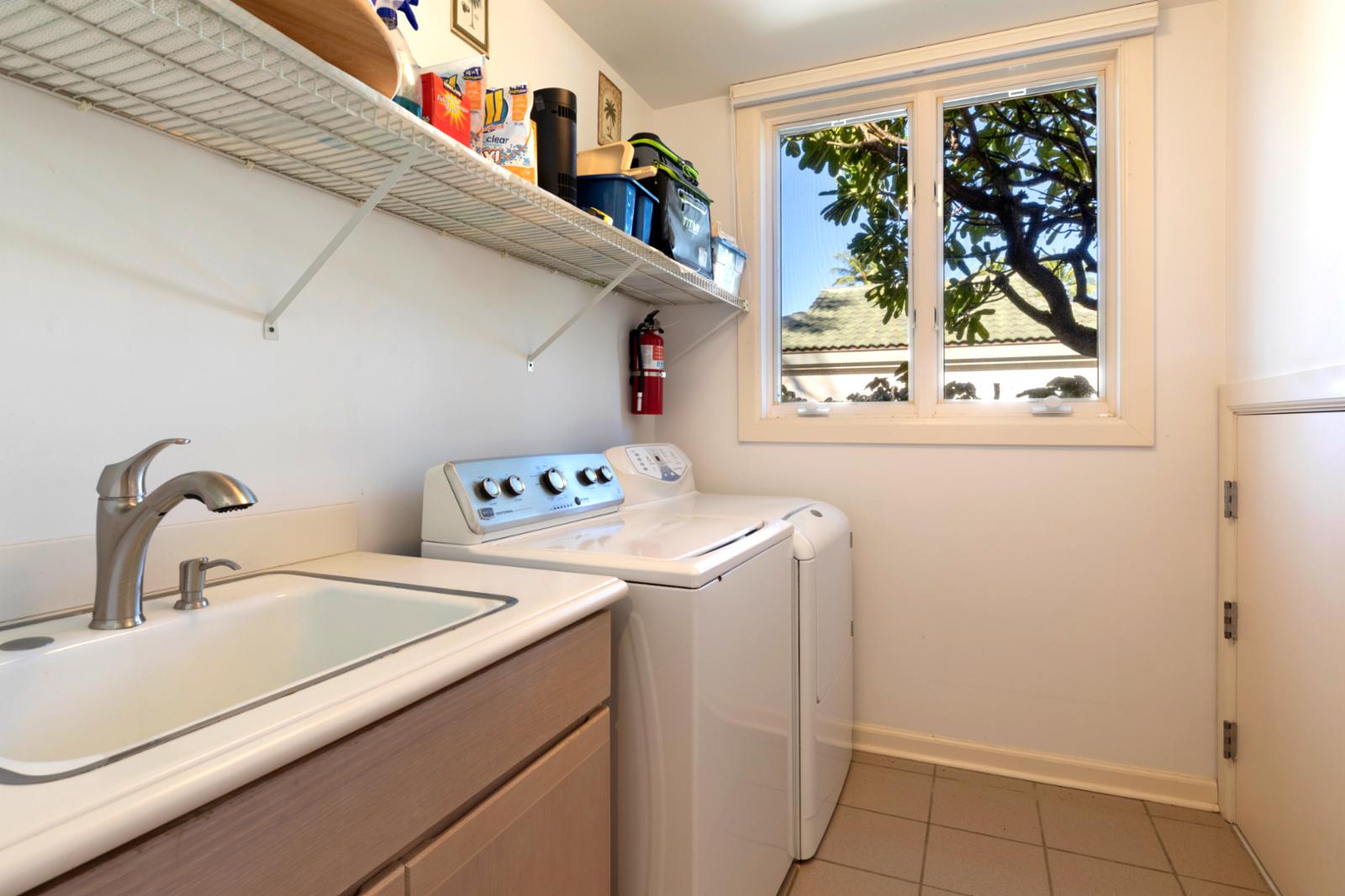 Bright laundry room with washer, dryer, utility sink, and garden view.