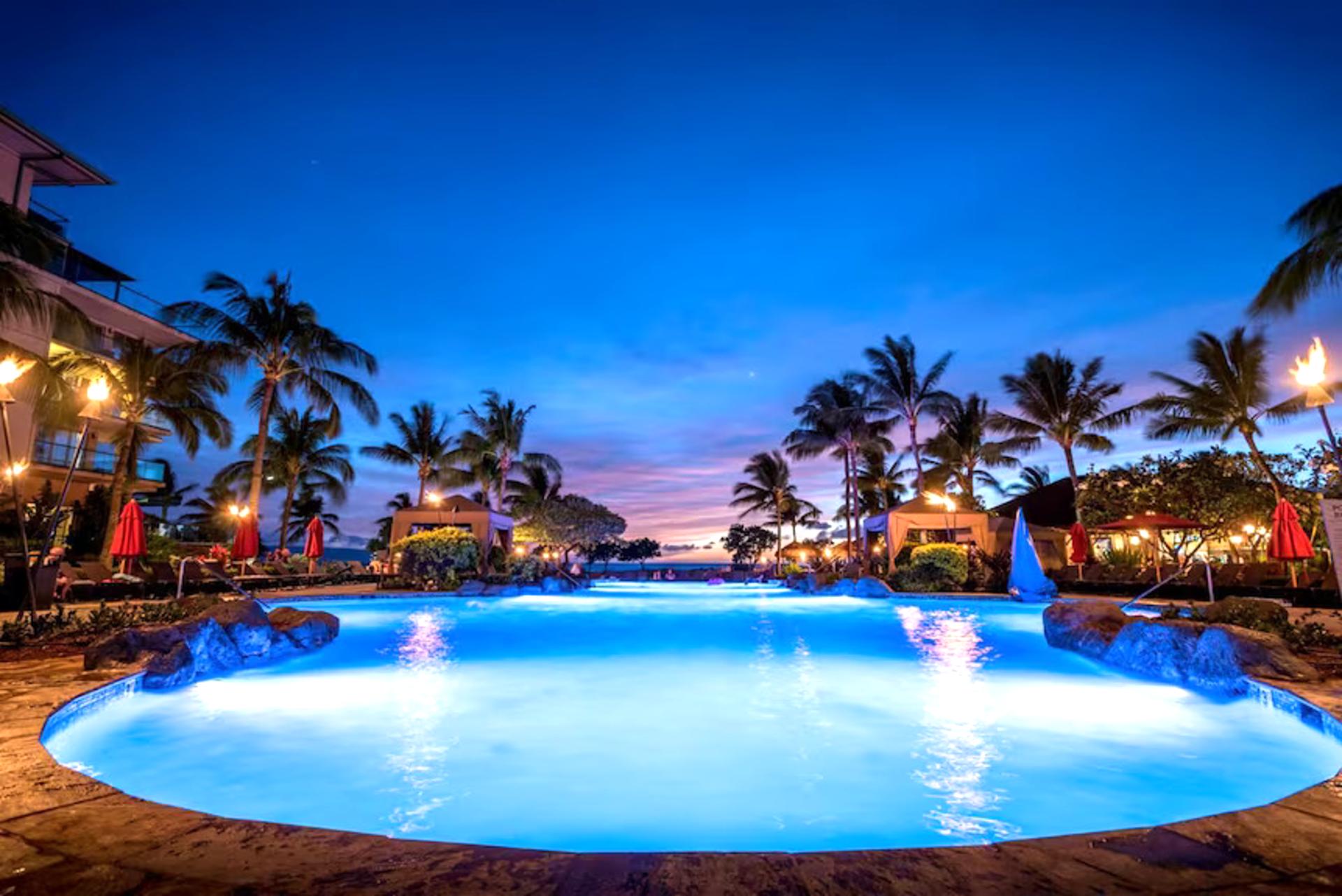 Tropical twilight glow over a serene, torch-lit resort pool.