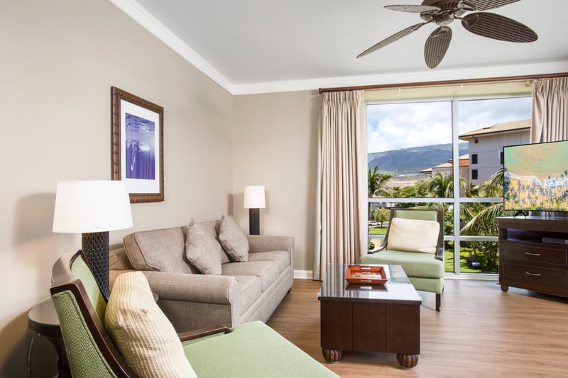 Relax in a sunlit living room with plush seating, warm tones, and views of lush palms and island skies