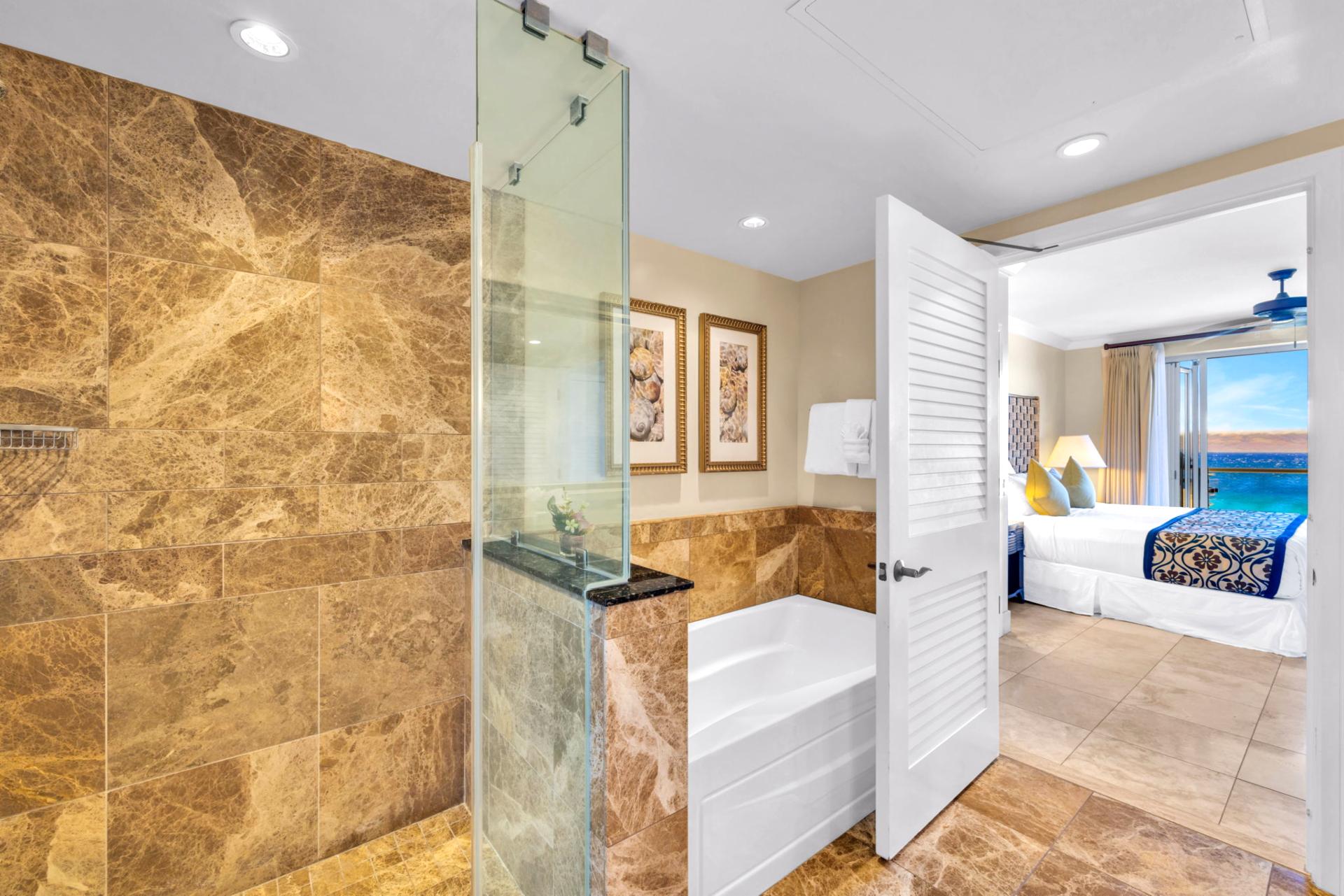 The guest bedroom ensuite bath features a soaking tub and a glass walk in shower with elegant stone tile