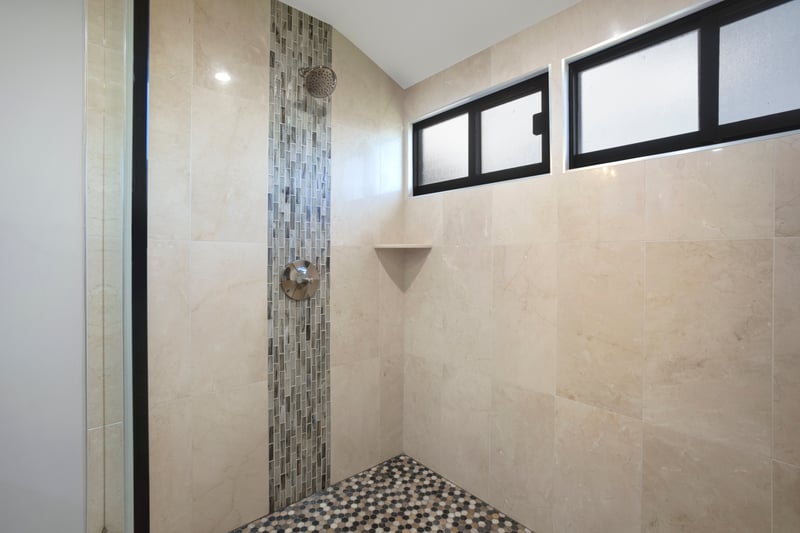 A frameless glass enclosure showcases the beautiful mix of textures and tones in the oversized walk-in shower