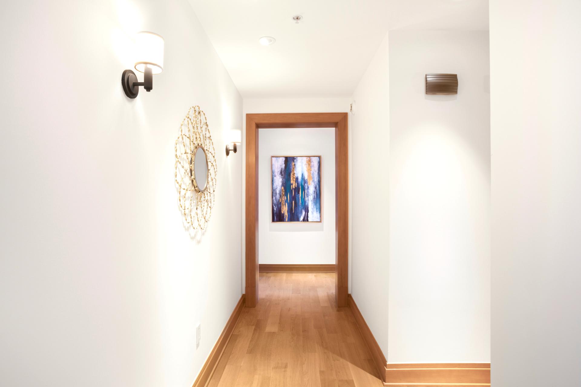 This softly lit corridor leads you into comfort, blending modern art, warm wood, and golden accents with grace   