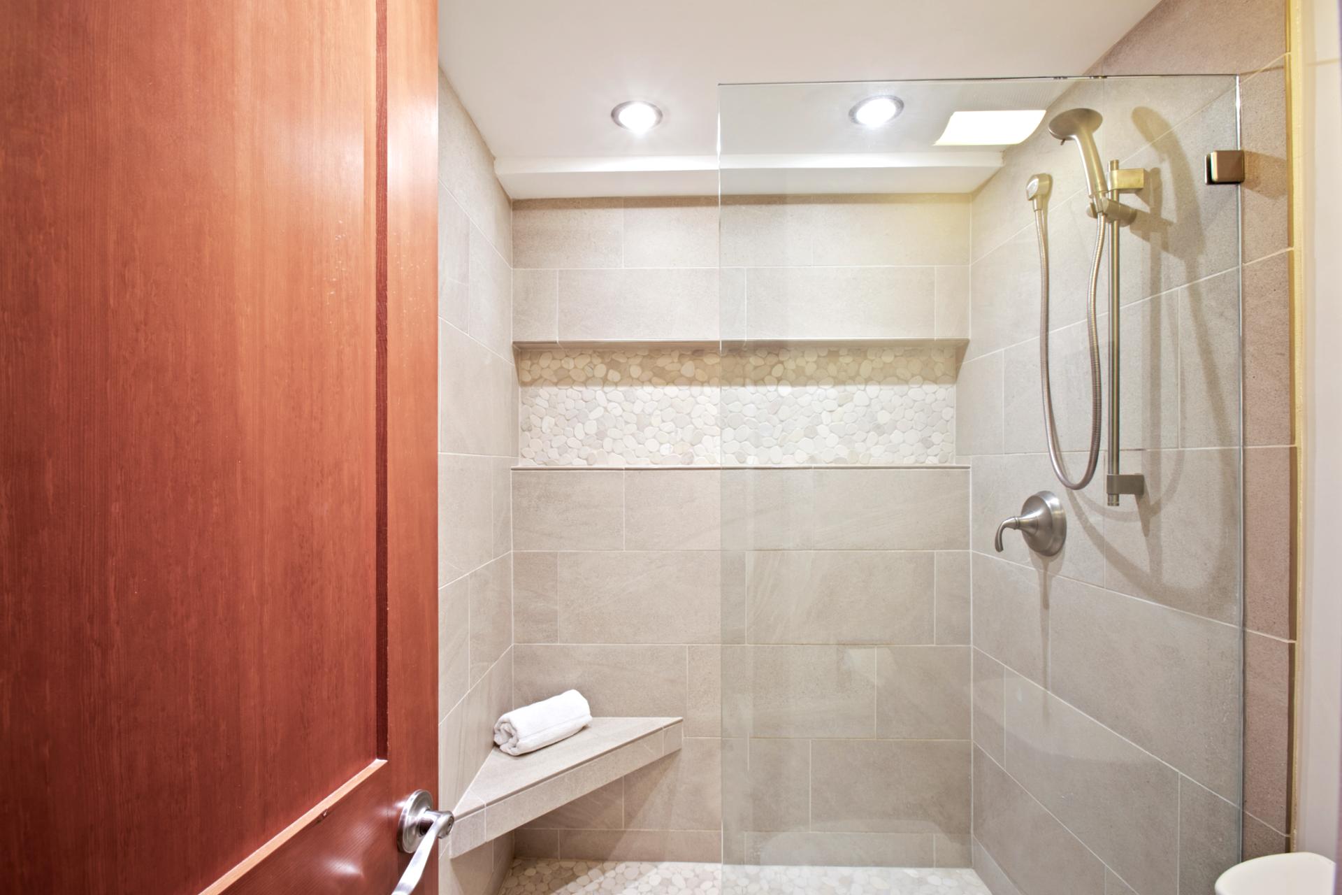 The walk-in shower is wrapped in smooth sandstone tile, accented by a horizontal mosaic band and an angled bench for comfort WH2-661