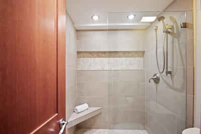 The walk-in shower is wrapped in smooth sandstone tile, accented by a horizontal mosaic band and an angled bench for comfort