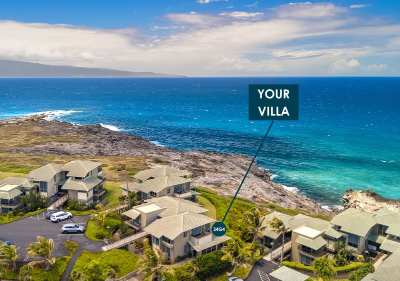Aerial coastline view from Kapalua Bay Villas showing Villa 34G4 perched above the turquoise water, with Molokai visible on the horizon.