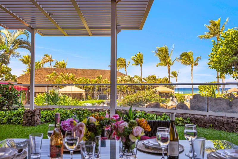 Pergola-covered lanai at Honua Kai HKH-150 — palm-lined grounds opening toward the resort pool and ocean beyond