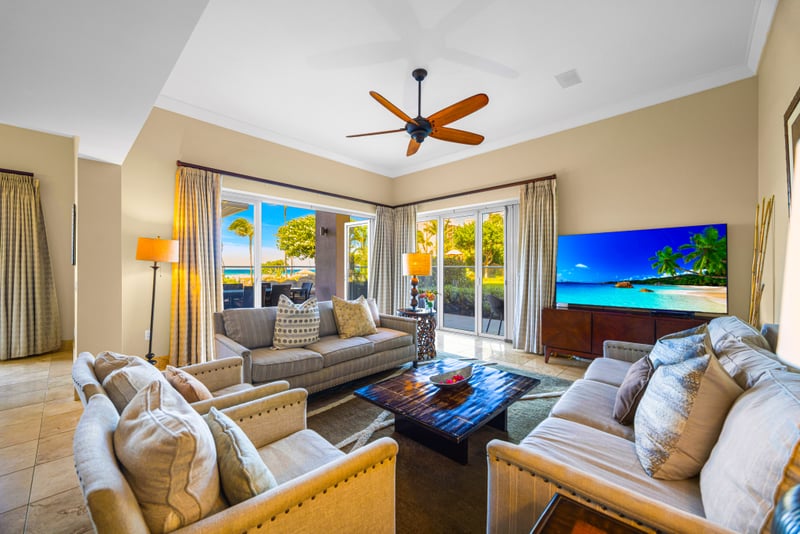 Living room at Honua Kai Hokulani 150 — plush seating for six, ceiling fan, and floor-to-ceiling sliders opening to the oceanview lanai