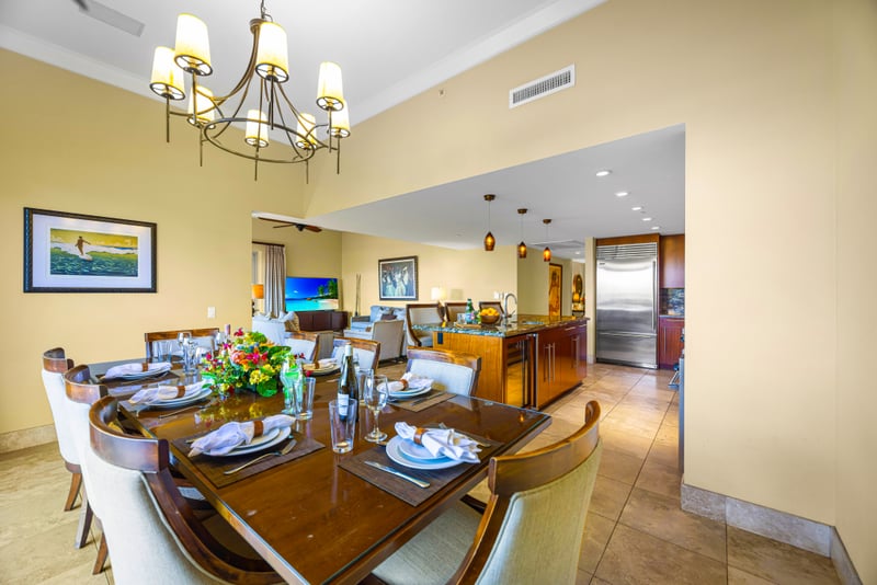 Dining room at Honua Kai HKH-150 — table for eight opening to the kitchen, wine cooler, and living room beyond