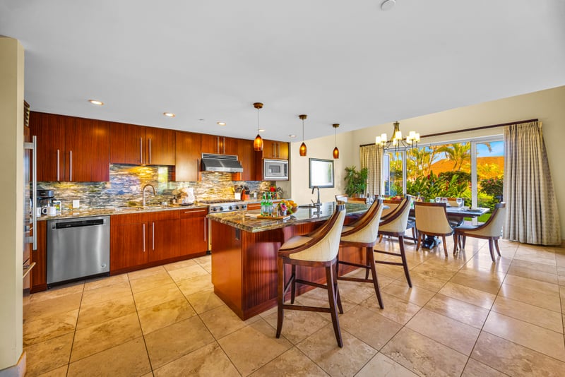 Open kitchen and dining at Honua Kai HKH-150 — granite island opens directly to the chandelier-lit dining room and garden views