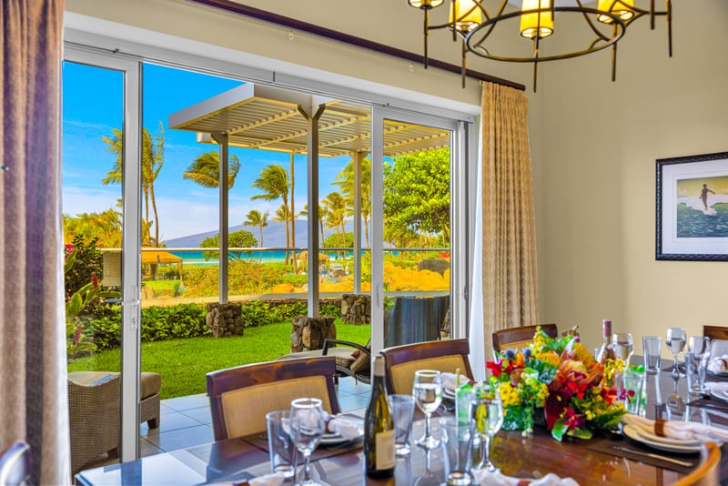 Dining room at Honua Kai HKH-150 — chandelier-lit table for ten with sliding doors to the pergola lanai and ocean beyond
