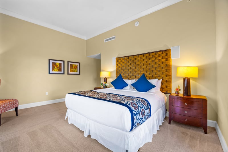 Primary bedroom at Honua Kai Hokulani 150 — king bed with a hand-woven headboard and reading lamps flanking dual nightstands