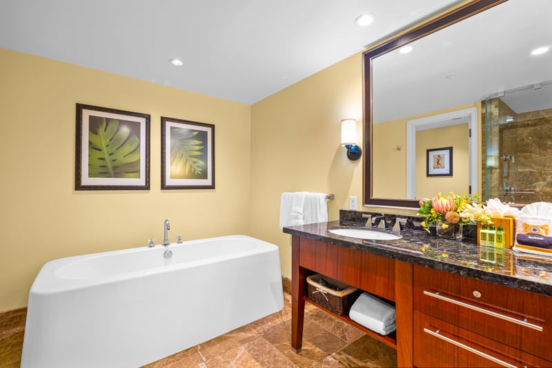 Primary bathroom at Honua Kai Hokulani 150 — deep soaking tub, glass-enclosed walk-in shower, and marble tile throughout