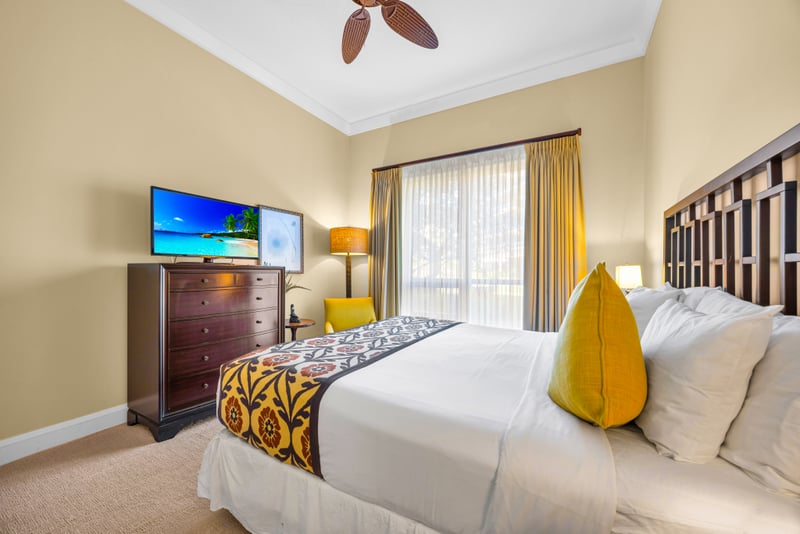 Guest bedroom at Honua Kai HKH-150 — smart TV, mustard accent chair, and warm island decor