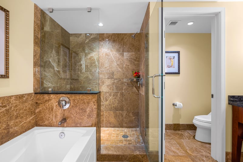Guest bathroom at Honua Kai Hokulani 150 — marble-tiled walk-in shower, soaking tub, and a private water closet