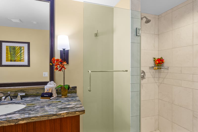 Guest bathroom at Honua Kai HKH-150 — frosted glass shower and fresh orchid accents on the vanity