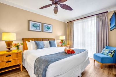 King bed, ceiling fan, and warm wood tones create a serene primary suite with private lanai access. HKH-305