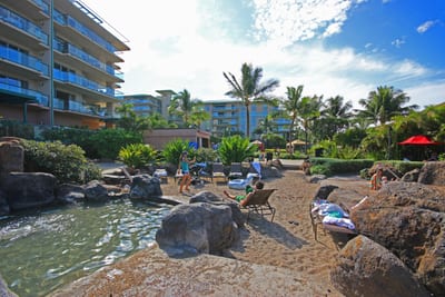 Tropical lagoon pool surrounded by lava rocks, palm trees, and red umbrellas under Maui’s signature sky