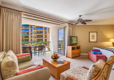 Spacious living area with ceiling fan, flat-screen TV, and warm island decor steps from the private lanai