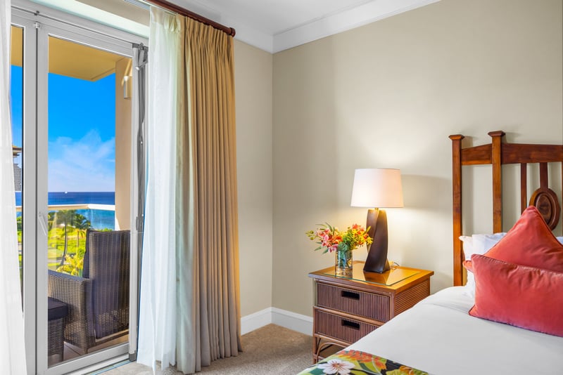 Primary bedroom with warm wood accents, King bed, and sliding door to the ocean-facing lanai.