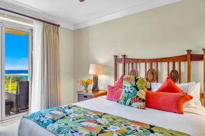 King bed with plush linens, ocean-view lanai access, and natural light in the primary suite. HKH-504