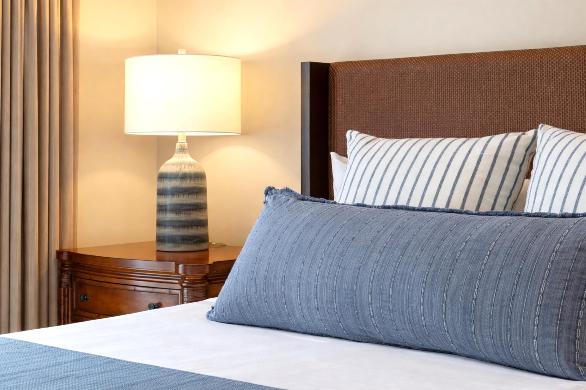 Plush bedding and layered pillows invite a comfortable night’s sleep in your Primary Bedroom, styled with soft coastal textures and warm lighting.