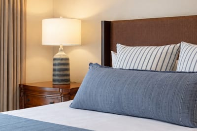 Plush bedding and layered pillows invite a comfortable night’s sleep in your Primary Bedroom, styled with soft coastal textures and warm lighting. HKH-515
